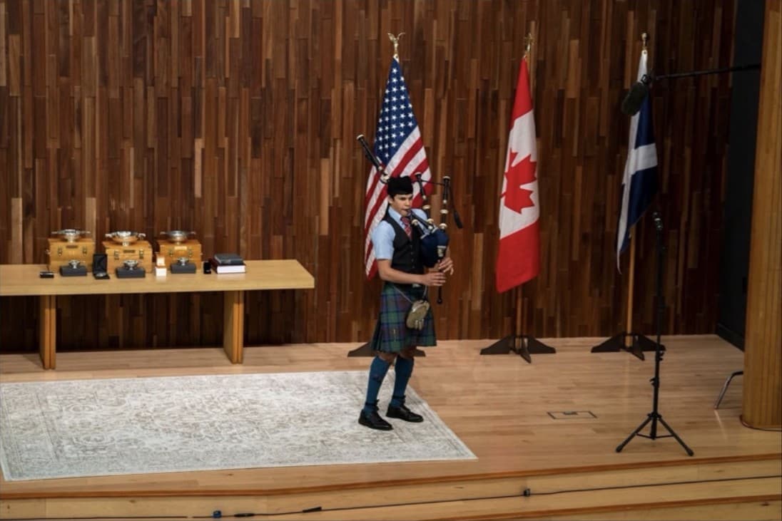 A solo piper performing on stage between international flags